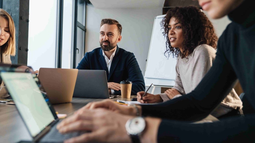 A group of professionals sitting around a table with laptops, engaged in a strategic discussion, focusing on business or data-related planning.