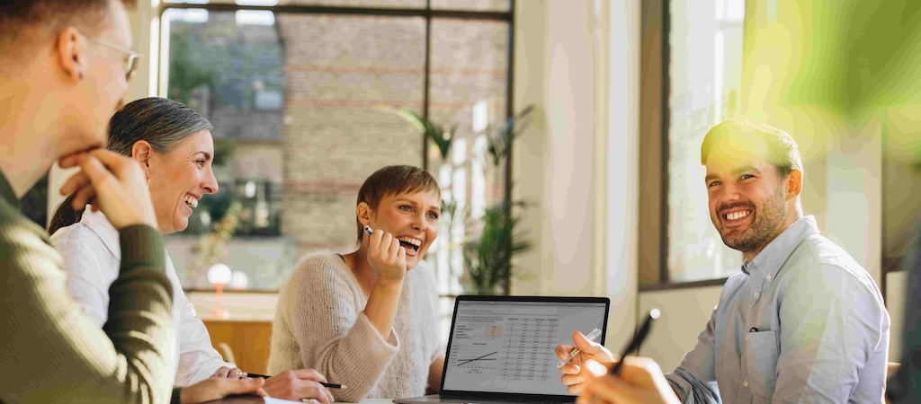 A team of colleagues gathered around a laptop, smiling and engaged in a lively discussion.