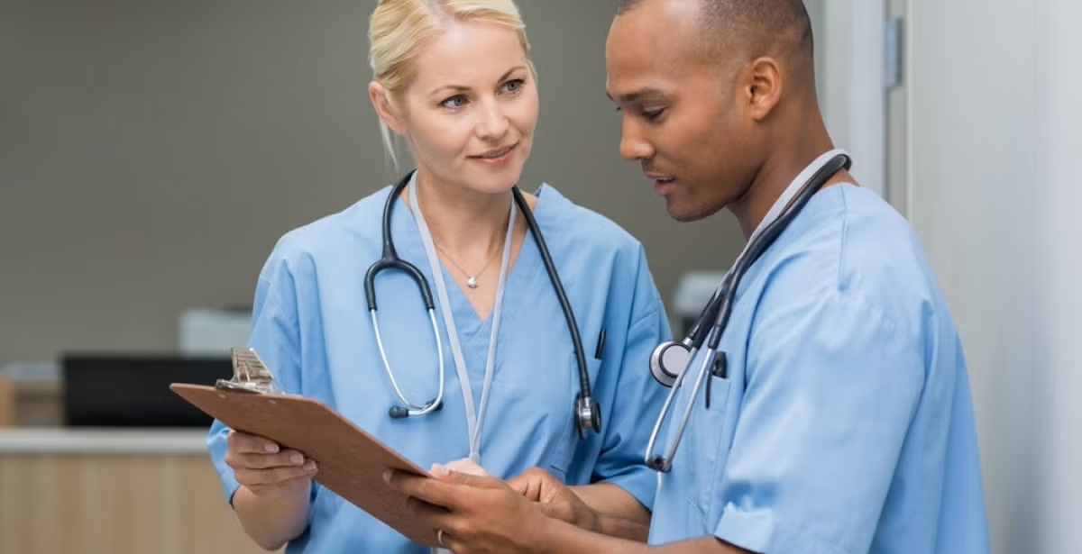 Two healthcare workers in scrubs reviewing a patient chart, both wearing stethoscopes.