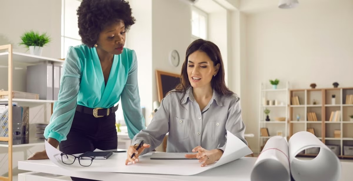 Two women working together on an architecture project, discussing blueprints.