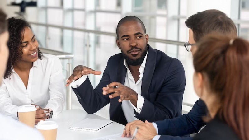A marketing director leading a team meeting, discussing plans and strategies with colleagues around a table.