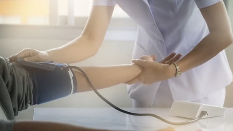 A nurse checking a patient’s blood pressure in a bright medical setting.