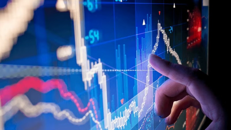 A hand pointing to data visualizations on a computer screen displaying financial graphs.