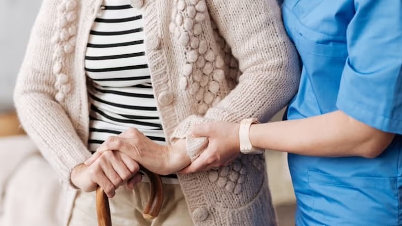 A healthcare worker holding a senior citizen's hand, symbolizing quality and safety in care services.