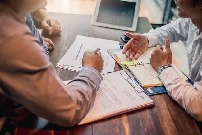 Business professionals working on documents and discussing reports at a meeting table.