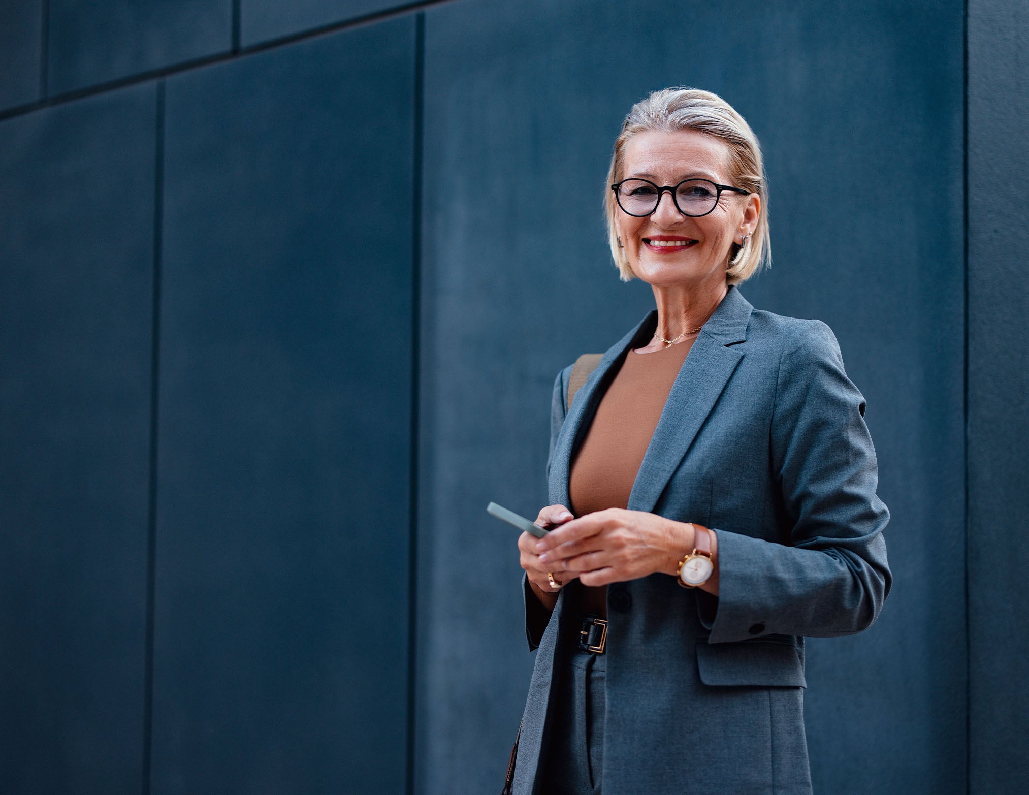 1. A professional woman in glasses and a suit holds a cell phone, appearing engaged in a conversation or task.