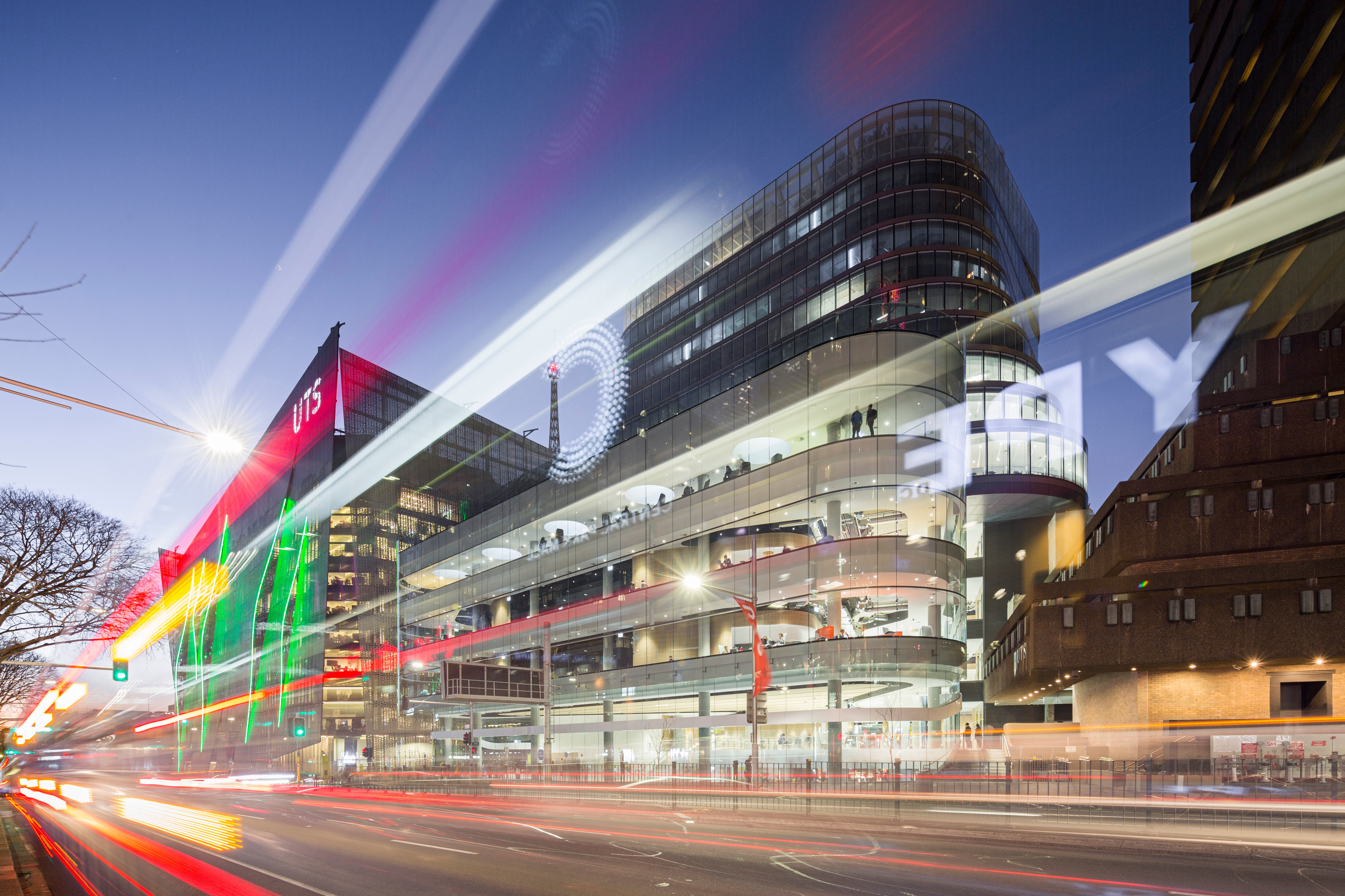 UTS city campus building at dusk with illuminated façade and light trails from passing traffic in the foreground.