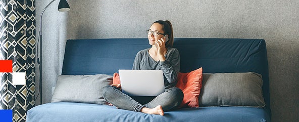 A woman wearing glasses is seated at a desk, engaged in a phone conversation.