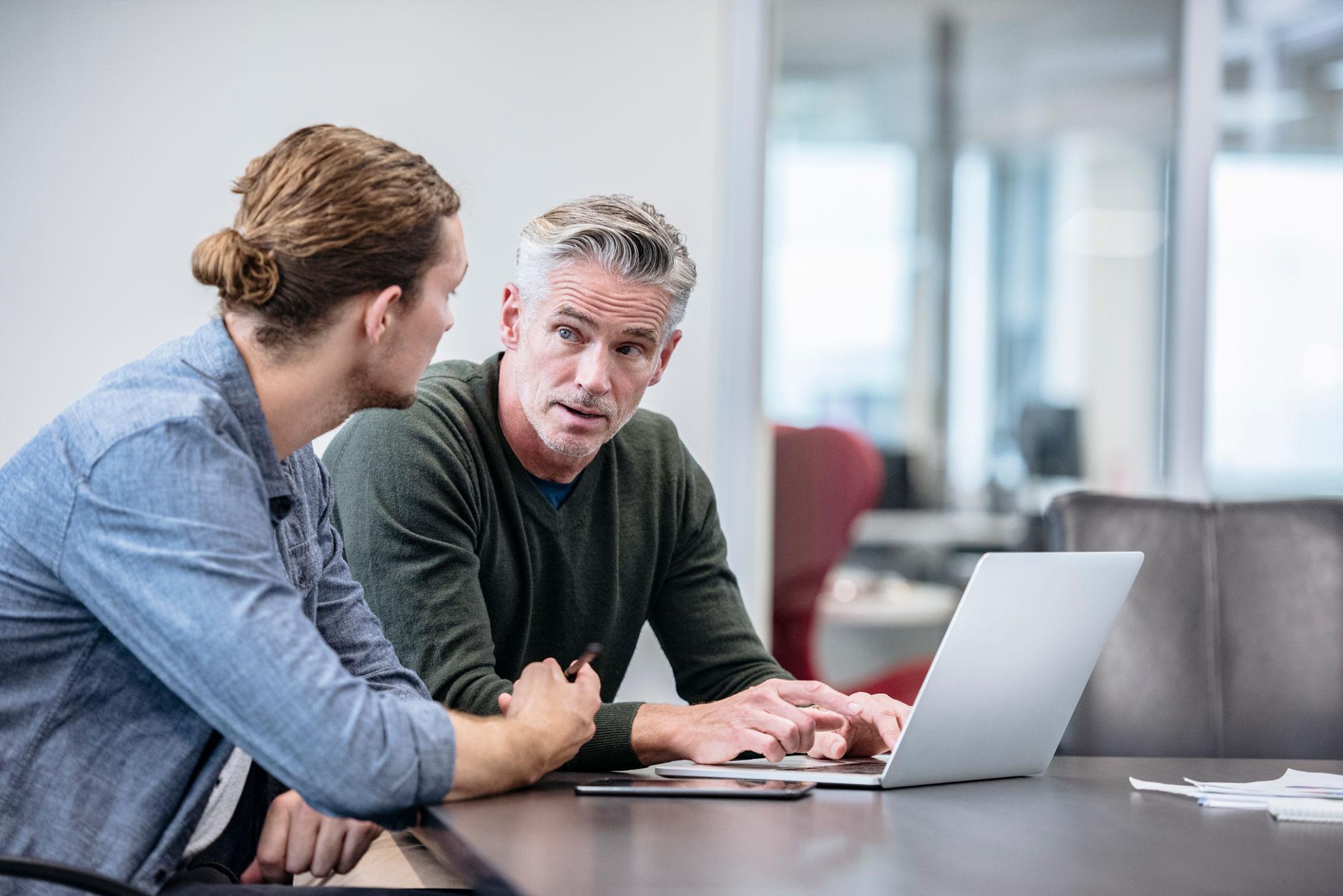 Two colleagues discussing work beside a laptop during a one-on-one workplace conversation.