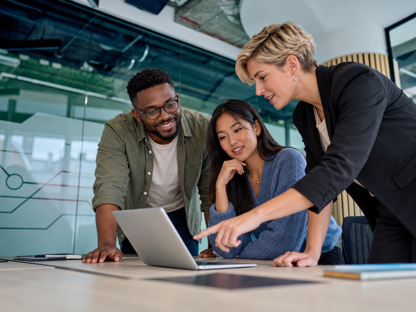 Three colleagues collaborating around a laptop during a workplace discussion.