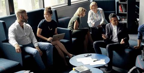 A group of professionals having a lively discussion in a meeting on their laptops.