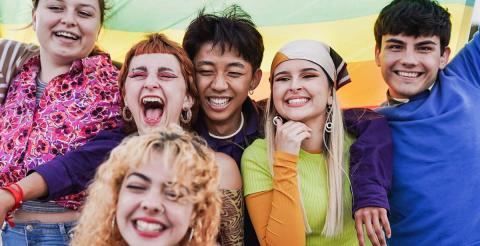 A joyful group of young people posing under a rainbow flag, celebrating diversity and inclusion.