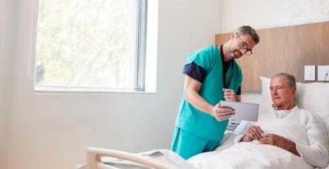 A healthcare professional showing information on a tablet to a patient in a hospital room.