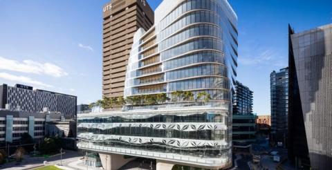 A modern UTS campus building with glass architecture and greenery on a terrace, set against a blue sky.