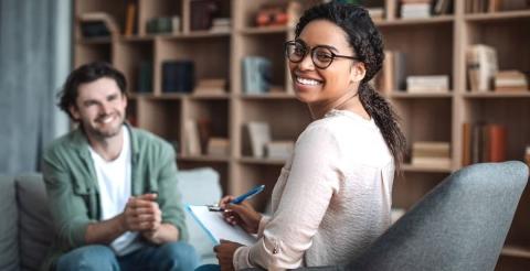 A smiling psychologist holding a clipboard in a consultation room.