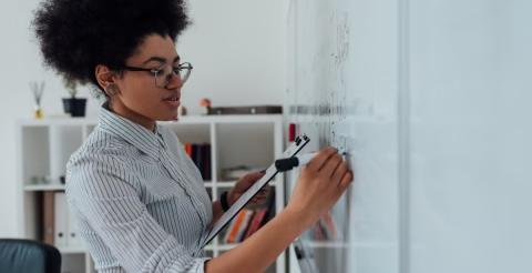 A woman holding a clipboard and writing on a whiteboard in an office setting.