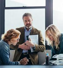 A business team reviewing documents and discussing ideas in a modern office with large windows.
