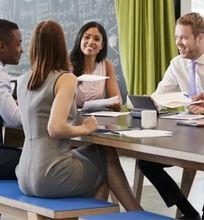 A group of five professionals collaborating around a modern conference table, engaged in discussions with laptops and documents.