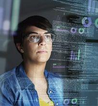 A woman with short hair and glasses, focused on data displayed on her computer screen in a dark room, analyzing complex visual data.