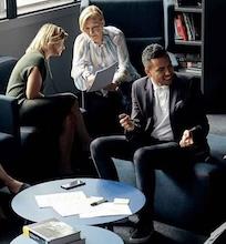 A group of professionals having a lively discussion in a meeting on their laptops.