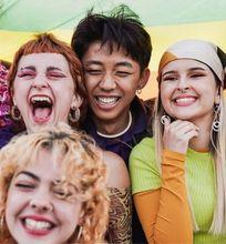 A joyful group of young people posing under a rainbow flag, celebrating diversity and inclusion.