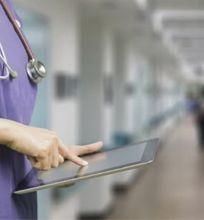 A healthcare professional in scrubs using a tablet in a hospital corridor.