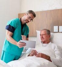 A healthcare professional showing information on a tablet to a patient in a hospital room.