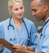 Two healthcare workers in scrubs reviewing a patient chart, both wearing stethoscopes.