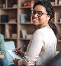A smiling psychologist holding a clipboard in a consultation room.