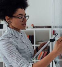 A woman holding a clipboard and writing on a whiteboard in an office setting.