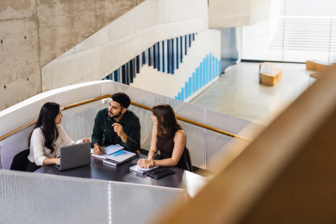 Three professionals discussing strategic communication around a table in a contemporary university-style learning space.