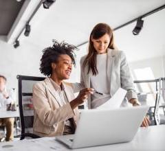 A general manager guiding a colleague on something they are working together on a laptop in an office environment.