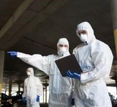 Three public health professionals in protective suits and masks standing and discussing safety precautions.