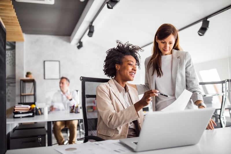 A general manager guiding a colleague on something they are working together on a laptop in an office environment.