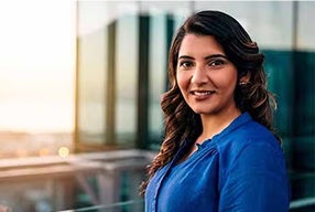 A woman in a blue shirt stands confidently in front of a vibrant city skyline, showcasing urban life and modern architecture.