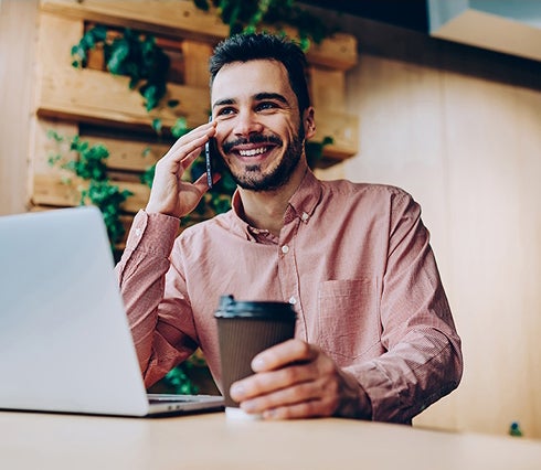 A man is speaking on the phone while holding a cup of coffee in his other hand, appearing engaged in conversation.