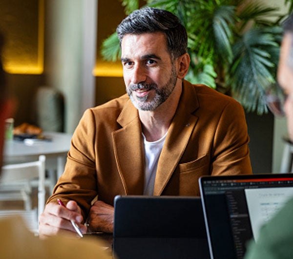 1. A man seated at a table with two other men, engaged in conversation and sharing ideas.