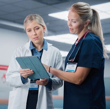 Two women in lab coats examining a tablet together, engaged in a discussion in a laboratory setting.