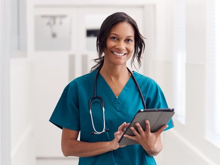 A smiling nurse stands holding a tablet computer, showcasing a friendly and professional demeanor in a healthcare setting.