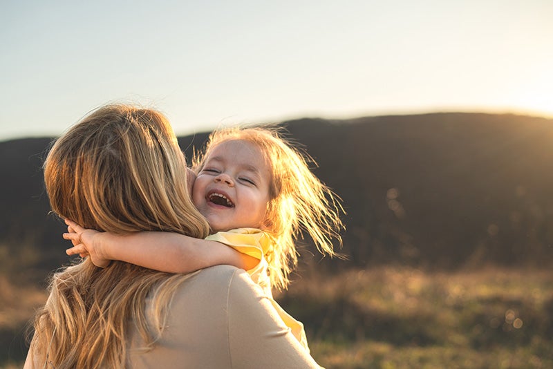 A woman cradles a child in a field, bathed in the warm glow of a sunset. 