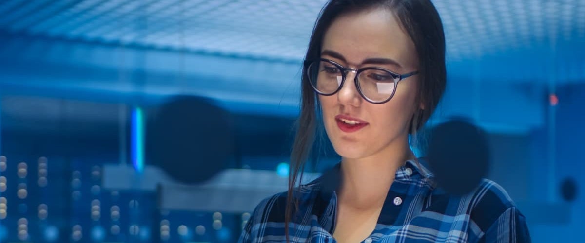 A woman with glasses wearing a blue shirt, smiling and looking directly at the camera.