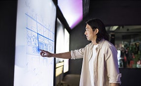 A man in an office pointing at a whiteboard filled with notes and diagrams.