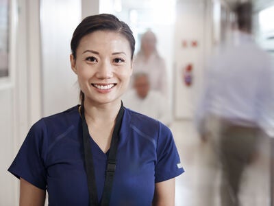 Portrait of smiling female nurse wearing scrubs in busy hospital corridor.