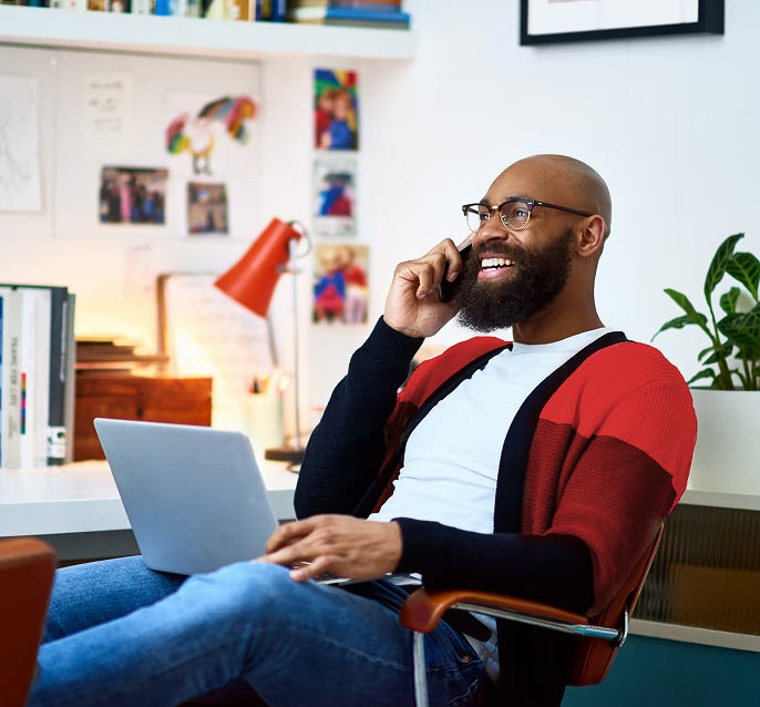 A bearded man sitting on a chair, engaged in a conversation on his phone.