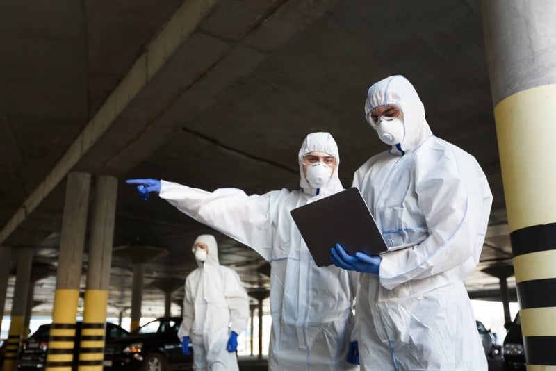 Three public health professionals in protective suits and masks standing and discussing safety precautions.